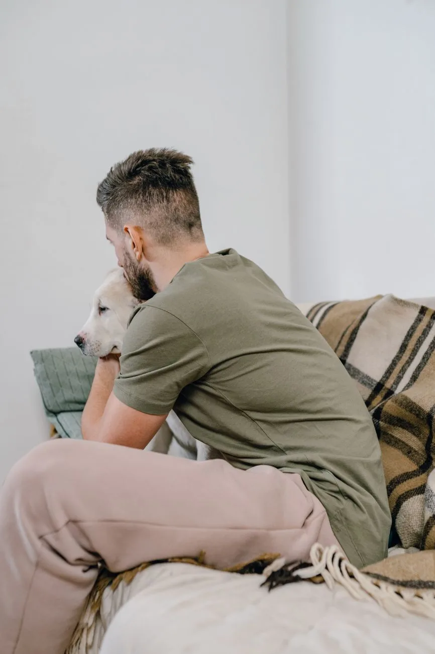 Man hugging his dog on a couch, seeking comfort and showing sorrow related to pet loss grief