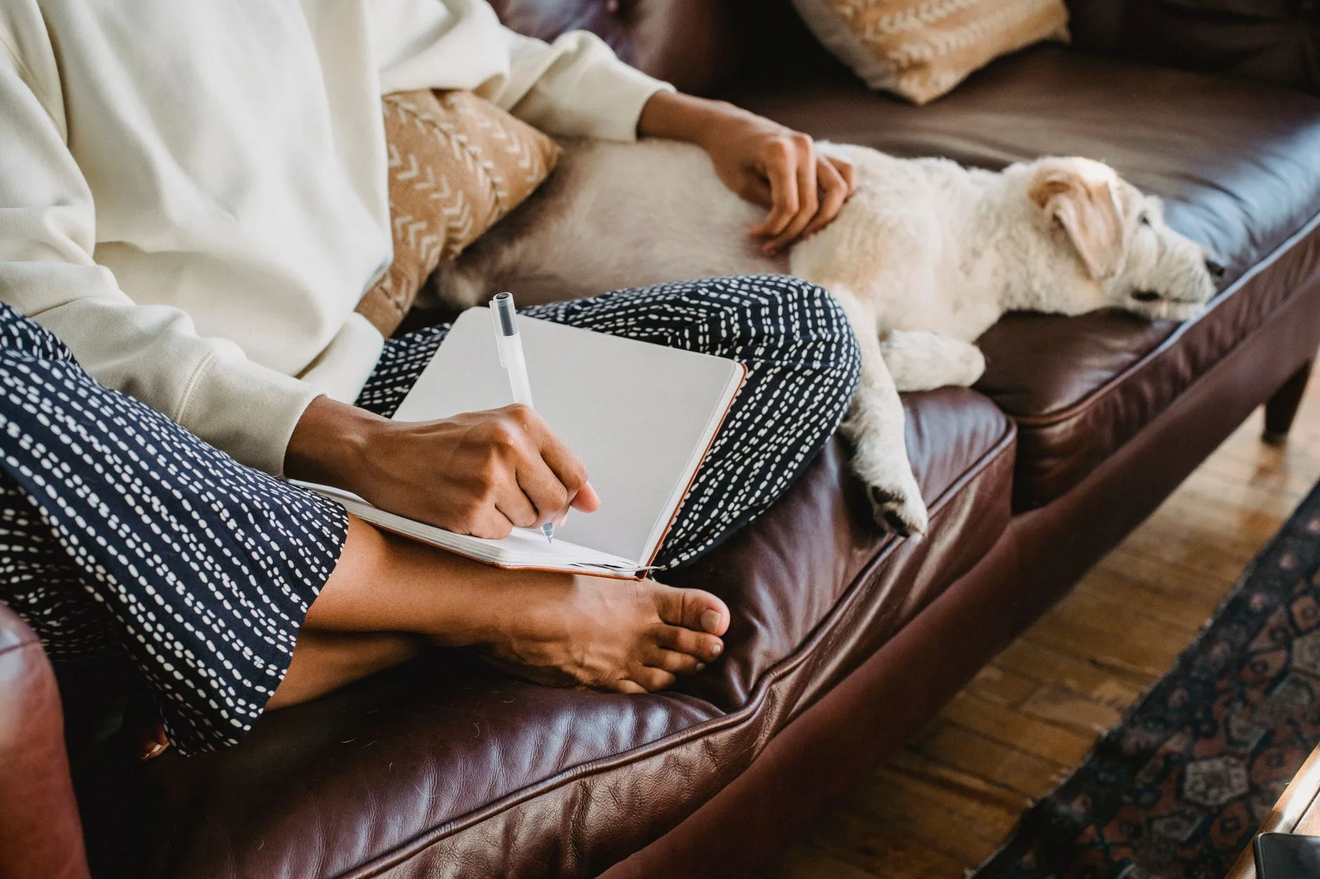Person journaling on a couch with their dog resting beside them, using pet grief journal prompts for emotional healing.